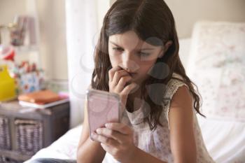 Young Girl In Bedroom Worried By Bullying Text Message