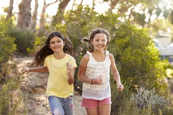 Two happy young girls running in a forest, close up