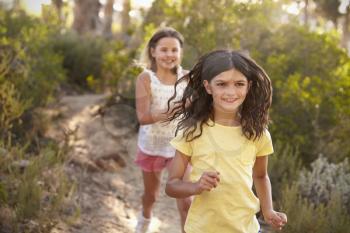 Two happy smiling girls running after each other in a forest