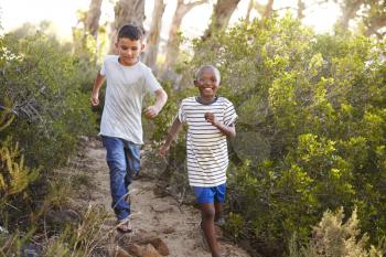 Two smiling young boys racing on a forest path