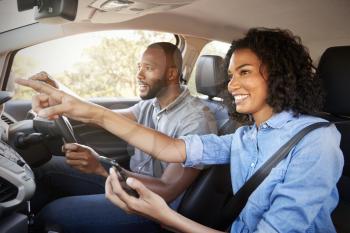 Happy couple in car on a road trip navigate with smartphone