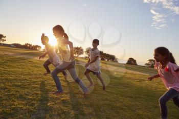 Four children running barefoot uphill in a park