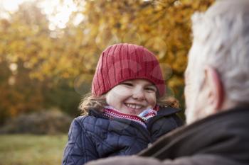 Grandfather Cuddling Granddaughter On Autumn Walk