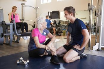 Senior Woman Discussing Exercise Program With Male Personal Trainer In Gym
