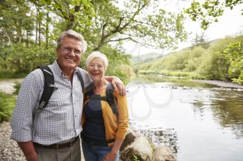 Portrait Of Senior Couple Hiking Along Path By River In UK Lake District