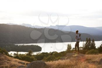 A young mixed race man standing alone on the rock, watching lake view, landscape