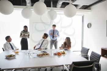 Businessmen And Businesswomen Meeting In Modern Boardroom Over Working Lunch