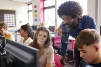 Male Teacher Helping Teenage Female High School Student Working In Computer Class