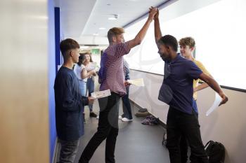 Excited Male Teenage High School Students Celebrating Exam Results In School Corridor