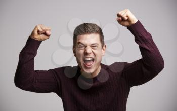 Portrait of a celebrating young white man with arms up