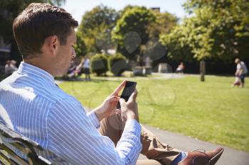 Businessman Outdoors Using Mobile Phone On Lunch Break In Park