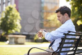 Businessman Sitting In City Park Looking At Smart Watch
