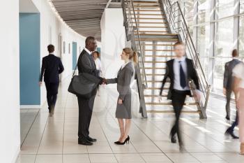 Businessman and woman shaking hands in a busy modern lobby