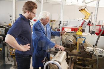 Senior engineer instructing apprentice at machine bench
