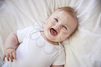 Overhead Shot Of Happy Baby Boy Lying On Parents Bed