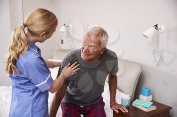 Nurse Helping Senior Man Out Of Bed On Home Visit