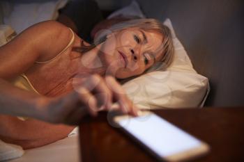 Sleepless Senior Woman In Bed At Night Checking Mobile Phone