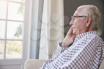 Senior man sits looking out of the window at home