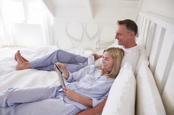 Couple Lying In Bed Looking At Digital Tablet Together