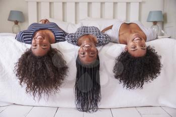 Three Teenage Sisters With Long Hair Lying On Bed At Home