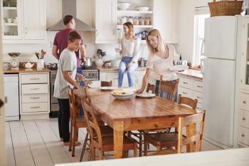 Family With Teenage Children Laying Table For Meal In Kitchen