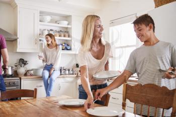 Family With Teenage Children Laying Table For Meal In Kitchen