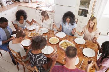 Two Families Saying Grace Before Eating Meal Together