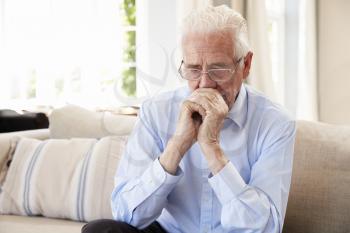 Senior Man Sitting On Sofa At Home Suffering From Depression