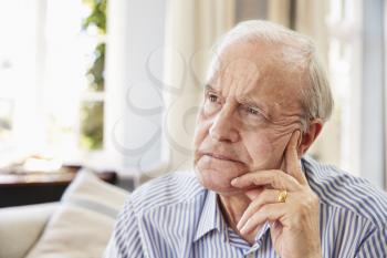 Senior Man Sitting On Sofa At Home Suffering From Depression