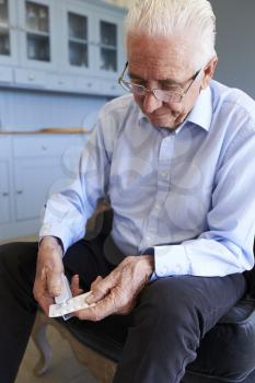Senior Man Using Pill Popper To Remove Medication From Packet