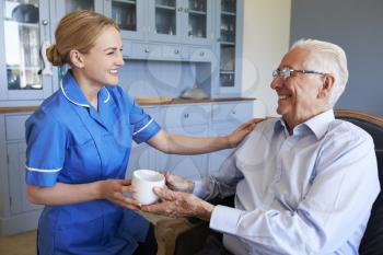 Nurse Giving Senior Man Cup Of Tea On Home Visit