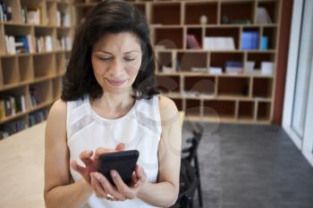 Middle aged female creative using smartphone in office