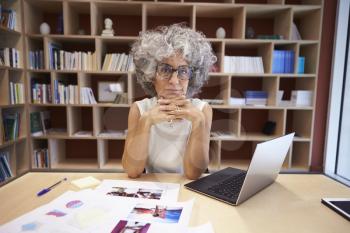 Senior businesswoman using laptop in office looks to camera