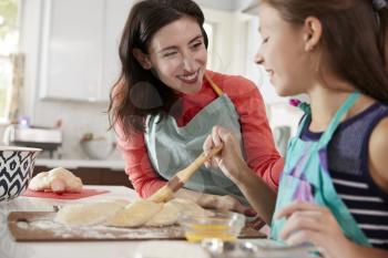 Girl brushing glaze on challah bread dough with her mum