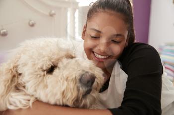 Young teen girl embracing pet dog on her bed, close up
