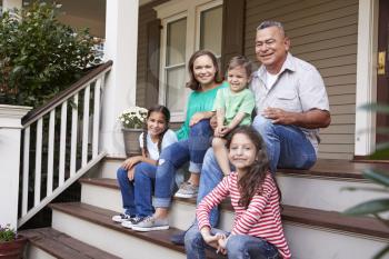 Grandparents With Grandchildren Sit On Steps Leading Up To Home
