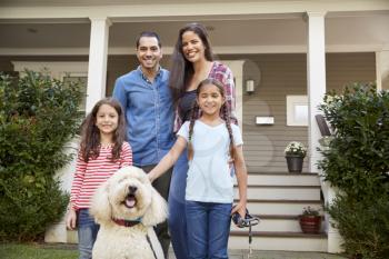 Portrait Of Family Standing in Front Of House With Pet Dog