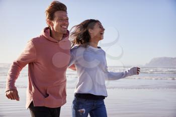 Couple Having Fun Running Along Winter Beach Together