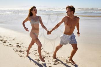 Couple On Summer Vacation Running Along Beach Together