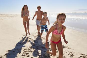 Family On Summer Vacation Running Along Beach Together