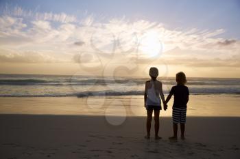 Rear View Of Children Holding Hands Silhouetted On Beach