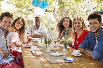 Six young adult friends dining outdoors smiling to camera