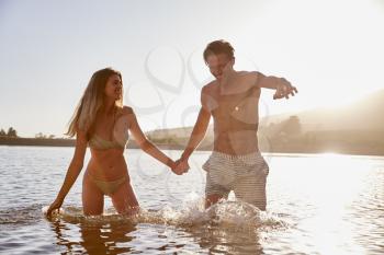 Young white couple holding hands in a lake at sundown