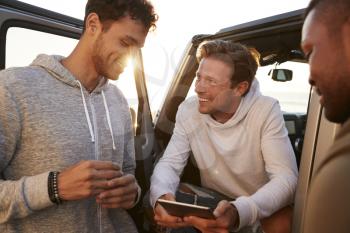 Three male friends on a road trip using a tablet, close up