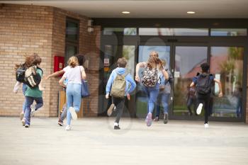 Group Of High School Students Running Into School Building At Beginning Of Class