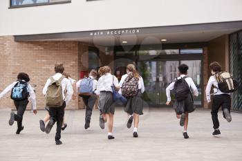 Group Of High School Students Wearing Uniform Running Into School Building At Beginning Of Class