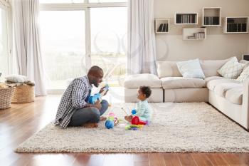 Black father and toddler son playing in sitting room