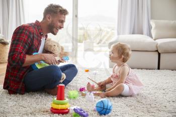 Father and young daughter play instruments in sitting room