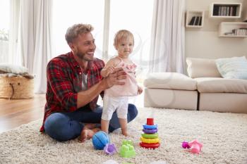 Young father helping toddler daughter stand in sitting room