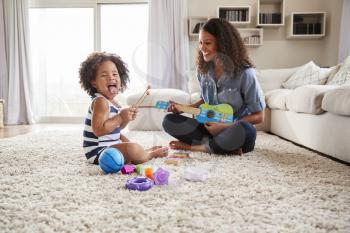 Young black mum plays ukulele with toddler daughter at home
